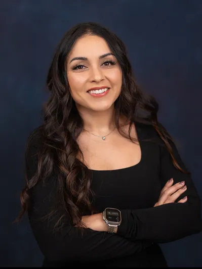 Raquel Ramirez smiling with folded arms against a dark background